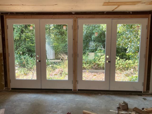 Two newly installed pairs of white French patio doors in a framed opening