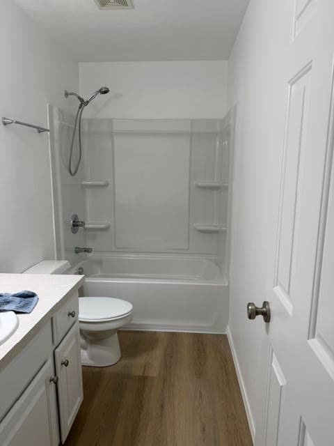 Remodeled bathroom with tub and shower surround, white vanity, and dark plank flooring