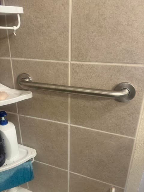 Stainless steel grab bar mounted on beige shower tile