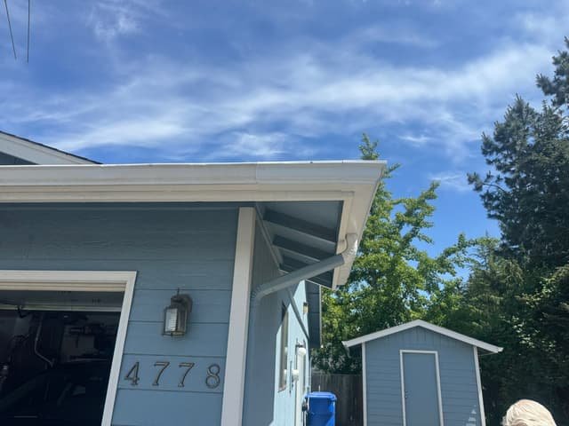 New white gutters and downspout installed on the corner of a light blue house