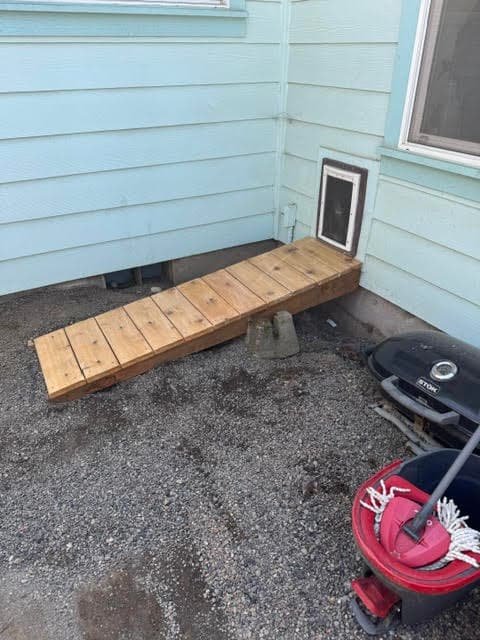Small custom wood ramp leading up to a pet door on light blue siding