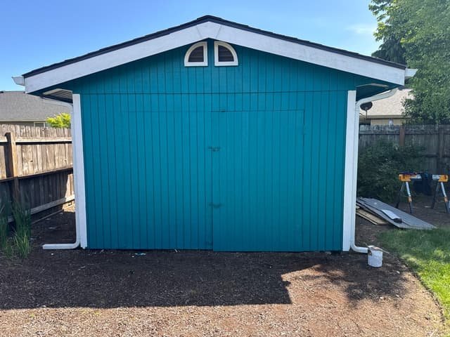 Backyard shed freshly painted teal with white trim, paint can still on the ground