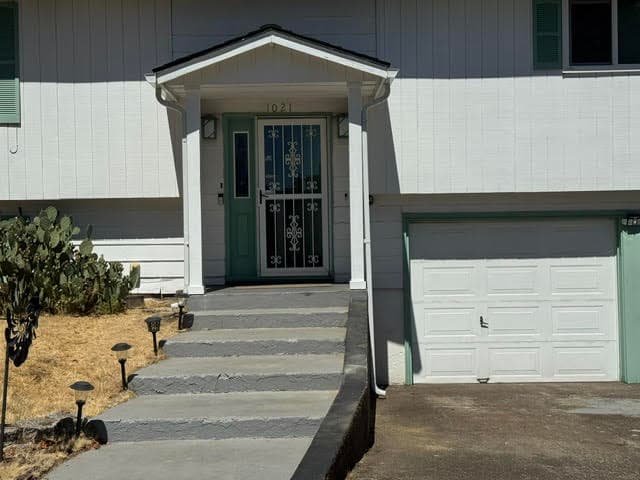 Front entry of a split-level house with security door, concrete steps, and garage