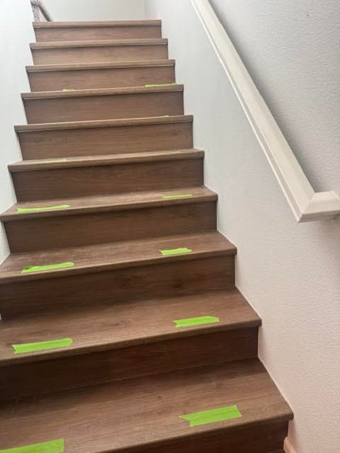 Staircase with new wood-look plank treads and white risers, painter's tape still marking steps