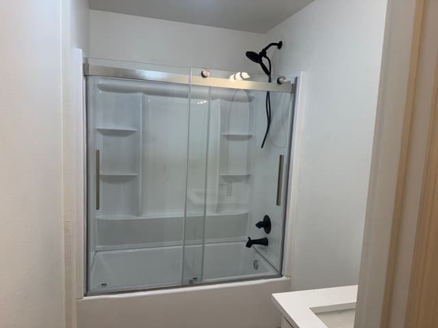 Tub and shower with new white surround, sliding glass door, and matte black shower fixtures