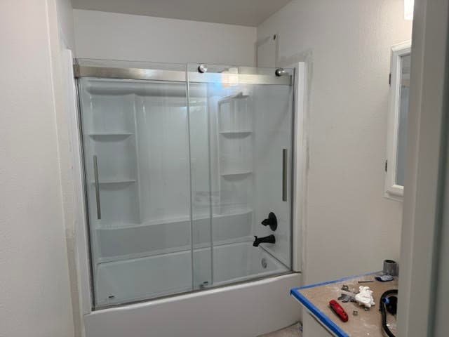 Tub and shower surround with a new sliding glass door mid-installation, tools on the vanity