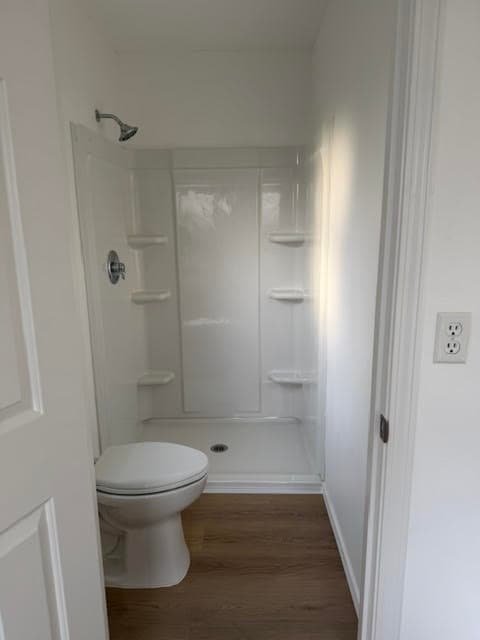 New white walk-in shower stall with built-in corner shelves next to a toilet